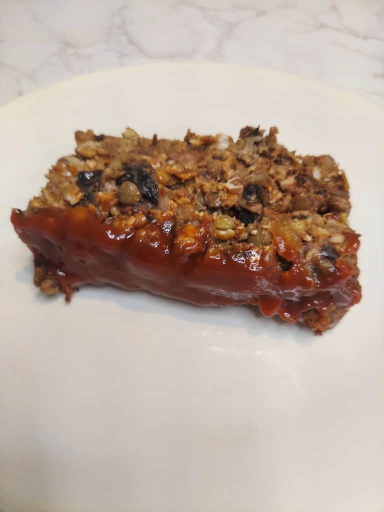 a slice of lentil mushroom loaf on a plate showing lentils and mushrooms inside