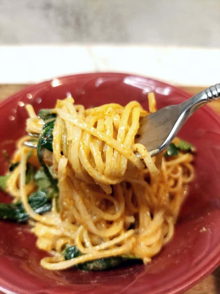 lifting vegan coconut curry noodles with a fork from the pan