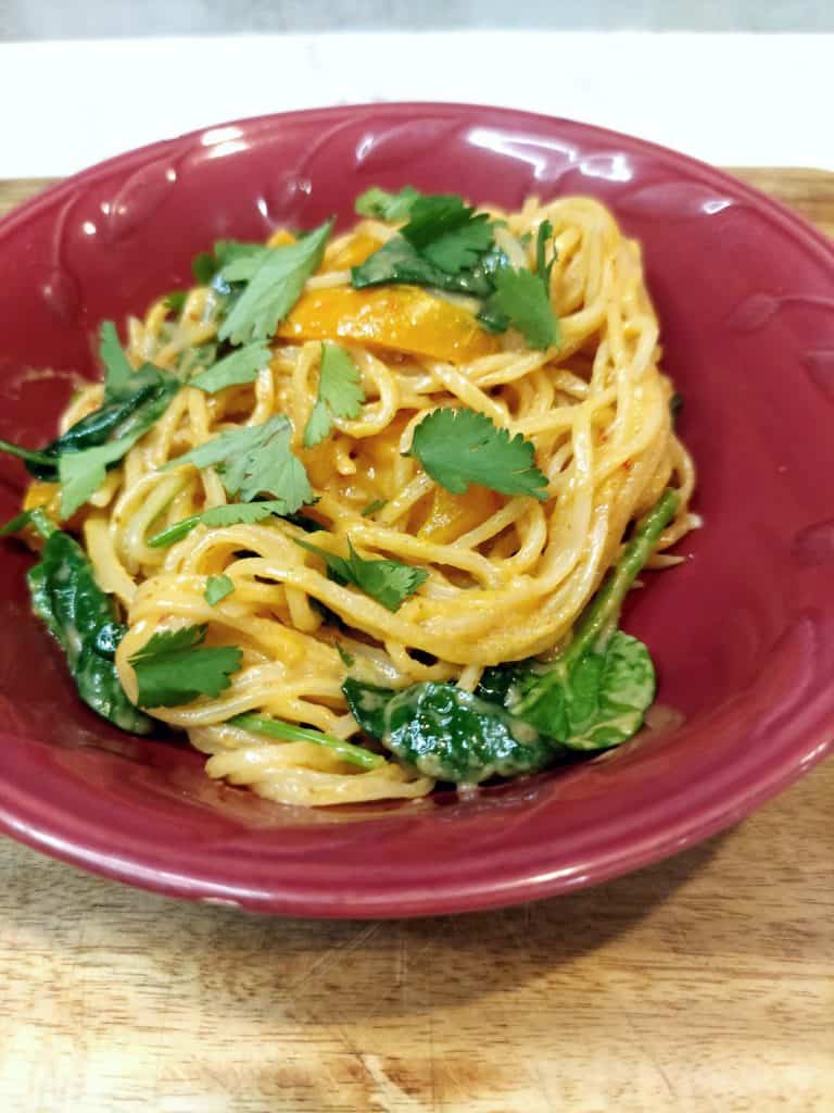 overhead view of rice noodles in creamy sauce with spinach and red bell pepper