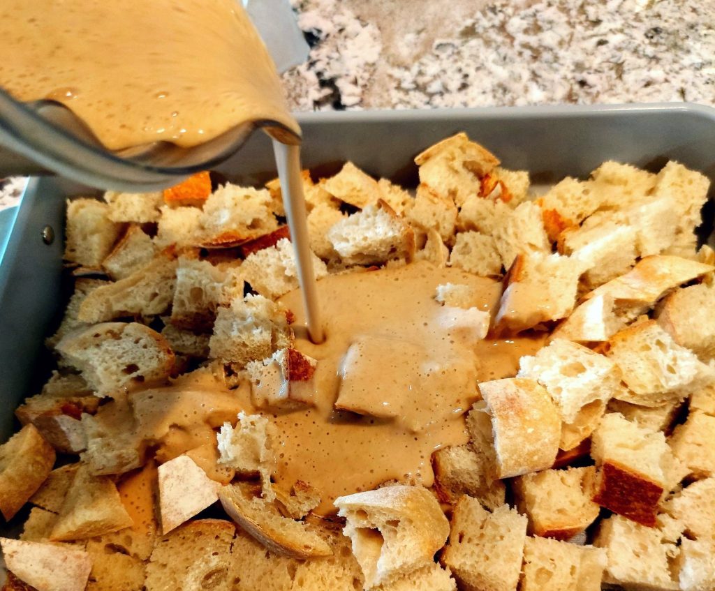 pouring blended banana protein custard over bread cubes in baking dish