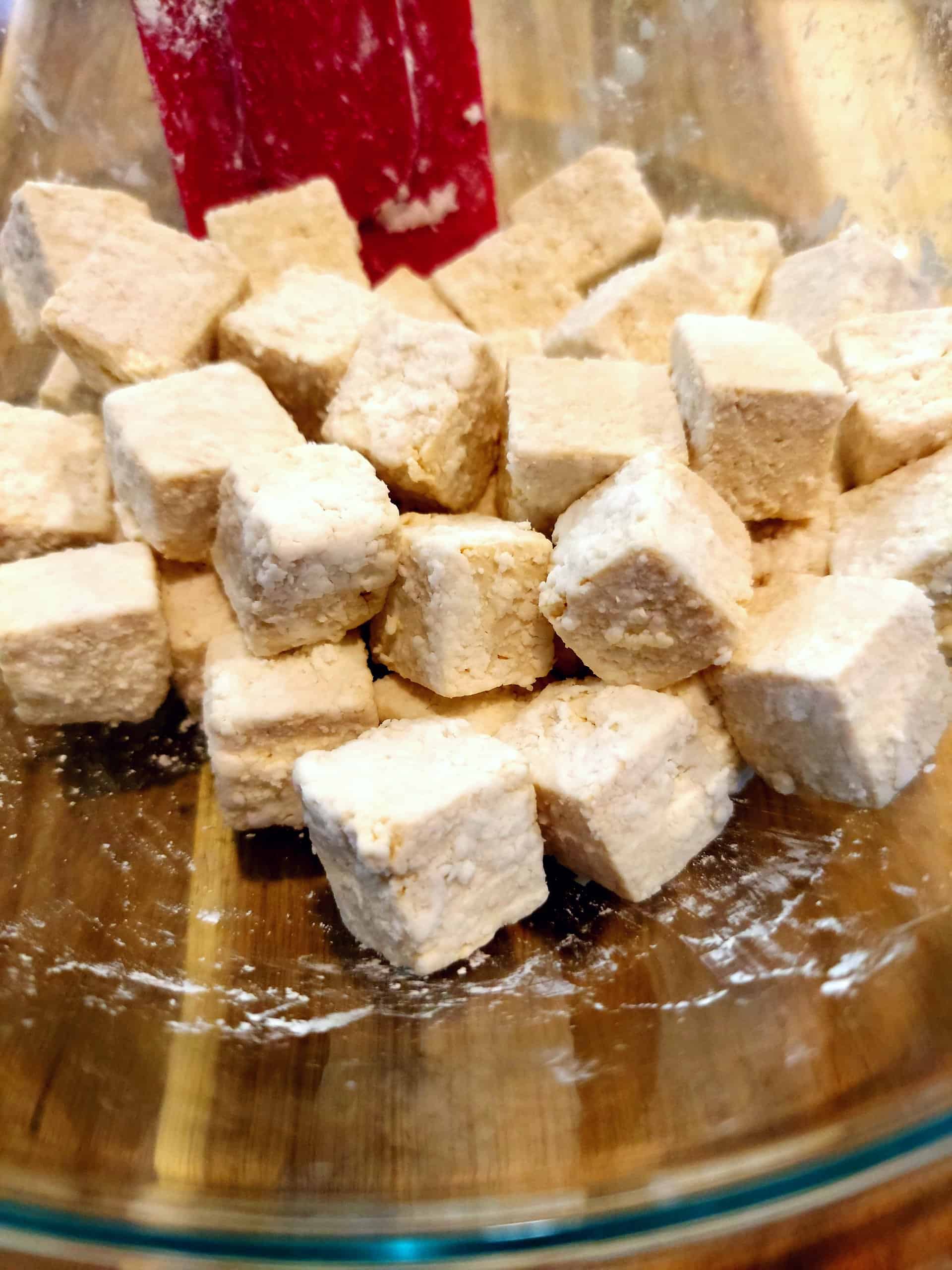 tofu cubes tossed in cornstarch in a glass mixing bowl